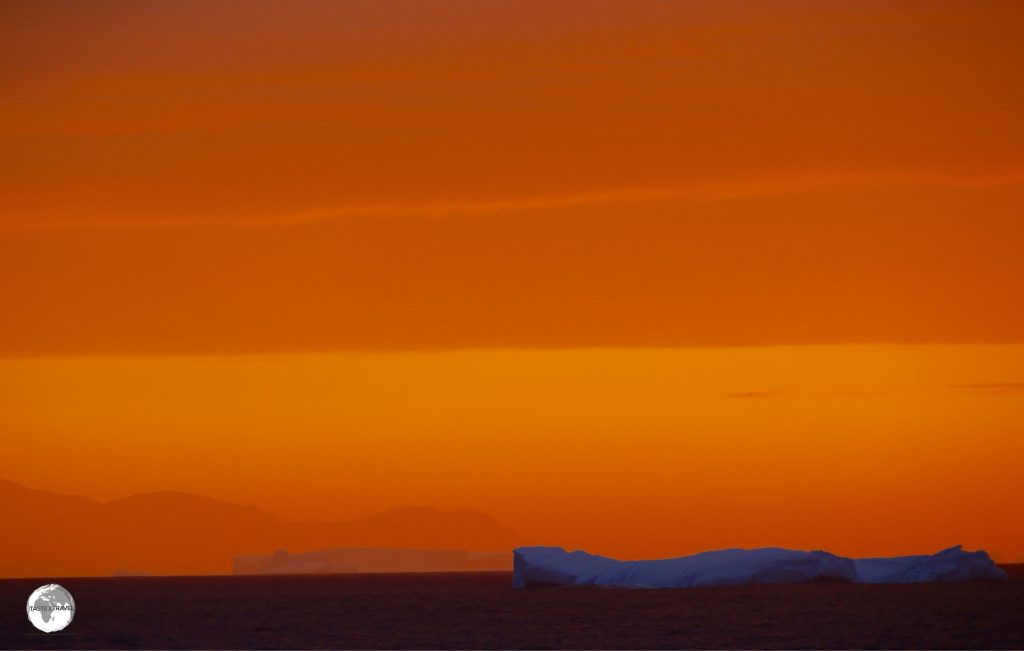 An iceberg illuminated against the sky of a setting sun.