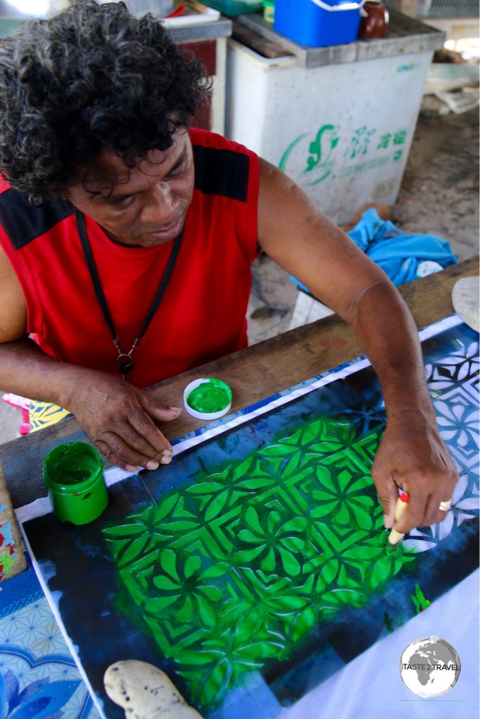 A craftsmen hand-painting a bed sheet.