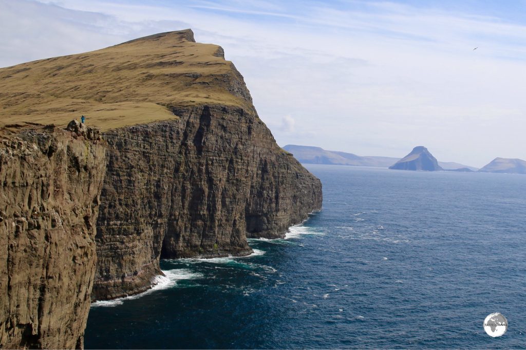 A lone hiker provides a sense of scale to the soaring cliffs on Vagur island.