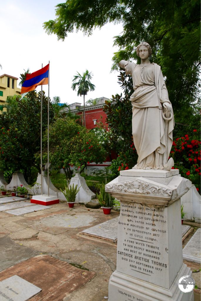 A statue on a gravestone with the Armenian flag in the background.