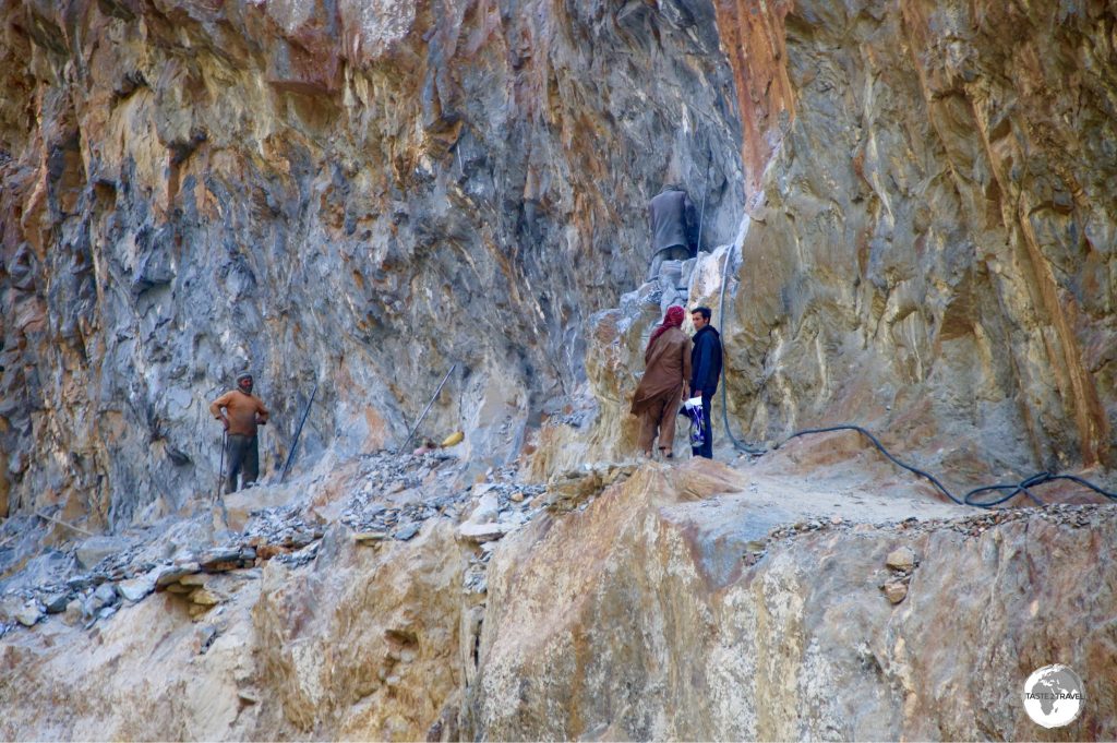 Afghan road workers carving the road out of a cliff face using a single jackhammer.