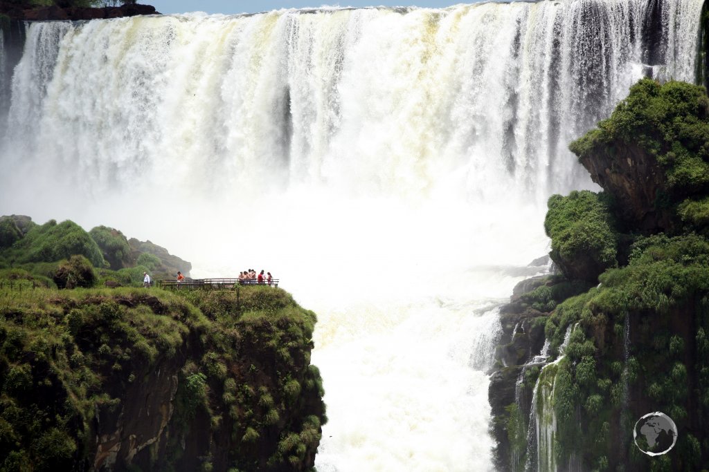 Looking towards the thundering Devils Throat at Iguazú Falls, with tourists visible on the Brazilian side of the falls.