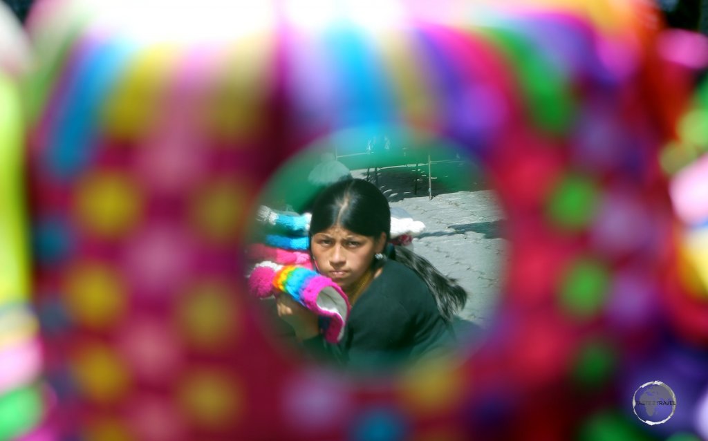 An Otavaleño native Indian hat vendor, reflected in a mirror which is attached to one of her colour, hand-woven hats, at the Otavalo craft market, Ecuador.