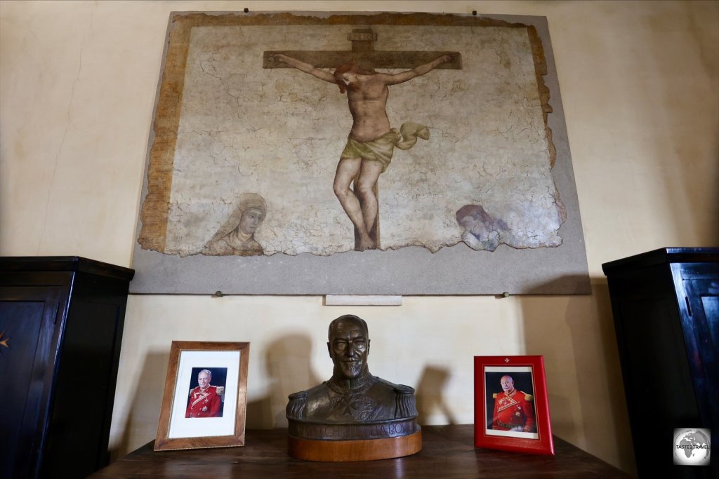 Photos of two former Grand Masters of the Order lie on a table beneath a painting of Christ at the A Magistral Throne inside the Hall of the Loggetta at the Casa dei Cavalieri di Rodi..
