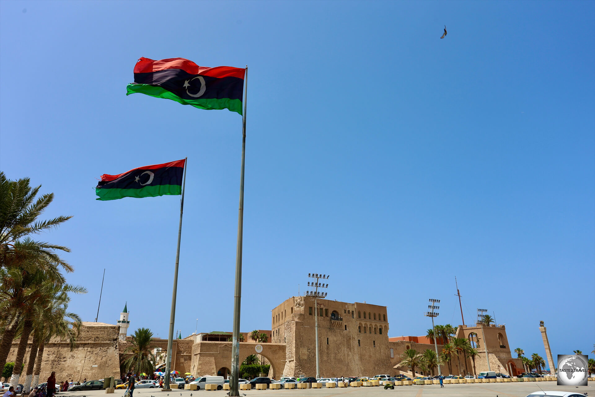 Libyan flags, flying over Martyrs' Square in Tripoli, with the walls of the medina and the Red Castle visible in the background.